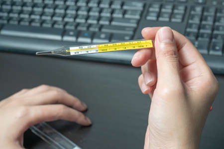 woman hand holding clinical thermometer on working desk,After using the clinical thermometer and worry about coronavirus spreadの写真素材