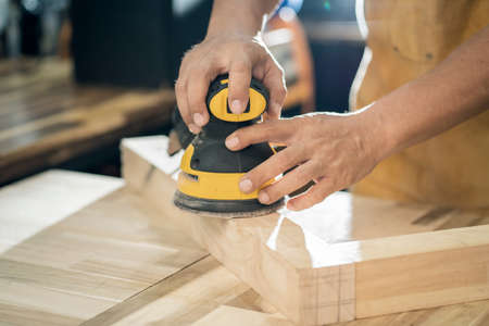 carpenter use random orbit sander or palm sander polishes wooden in the workshop ,DIY maker and woodworking concept. selective focusの写真素材