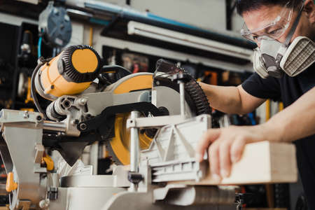 Carpenter cutting wooden with a miter saw or circular saw in shop, woodworking repair and...