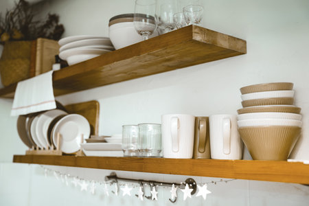 Wooden shelf with Glass, coffee cup, plate, bowl various cookware and decoration in kitchen. Hanging...