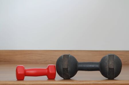 Old iron dumbbells and Red modern dumbbells on a wooden floor
