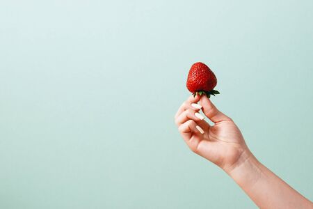 Woman holds strawberry in hand on front of grey-blue background.の写真素材