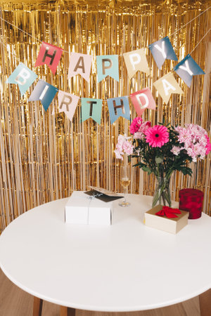 Decorations of "Happy Birthday", cake, presents and bouquet of flowers on the table and golden background. Preparation for the celebration of birthday, background for a banner for an advertisementの写真素材