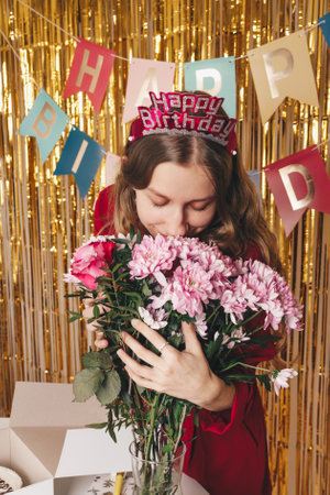 Beautiful girl smells bouquet of flowers at her birthday party. Blonde girl with flowers on the...