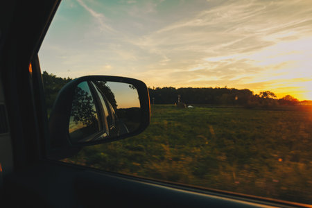 View on the road in the side mirror in front of the meadow at sunset. Beautiful view from the car to the field. Travel concept, adventures on the holidaysの写真素材
