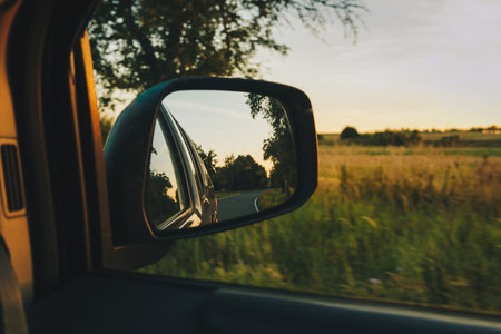 View on the road in the side mirror in front of the meadow at sunset. Beautiful view from the car to the field. Travel concept, adventures on the holidaysの写真素材