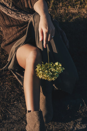 Beautiful young woman is sitting in the meadow with a bunch of flowers in her hand. End of summer,...