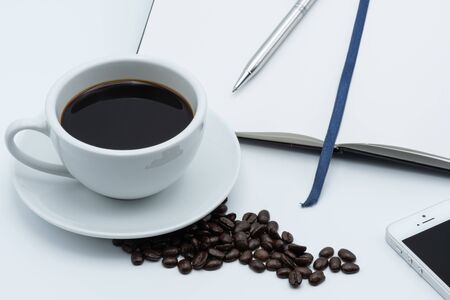 A cup of coffee on a white table with a book and penの写真素材