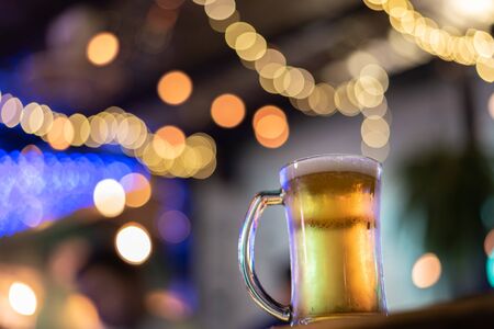 A glass of beer on wooden table in a cafe with blurry bokeh backgroundの写真素材