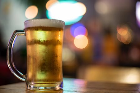 A glass of beer on wooden table in a cafe with blurry bokeh backgroundの写真素材