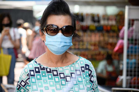 Bangkok, Thailand-Jun 13, 2020-An old woman wearing a sun glasses and a mask walks in the market.のeditorial素材