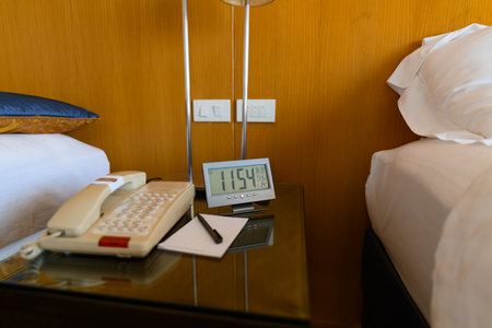A digital clock is placed on a bedside table with wooden walls and warm lighting.の写真素材