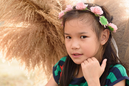 Portrait of an Asian girl wearing a pink flower headband in warm tones.の写真素材