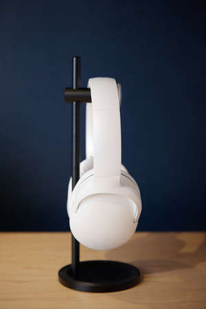 White wireless head large headphones stand on a wooden table on a black stand on a blue background...