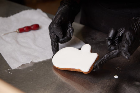 the cook holds a ready made cookie covered with white icing with his gloved handsの写真素材