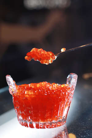 the cook holds a shiny spoon of red caviar over a bowl of red caviar side viewの写真素材