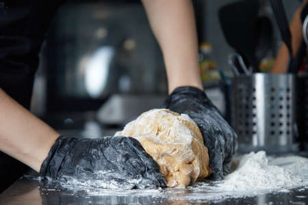 cook with gloved hands kneads dough on the table side viewの写真素材