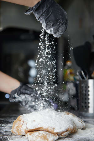 cook with gloved hands knead the dough and sprinkle it with flour on the table side viewの写真素材