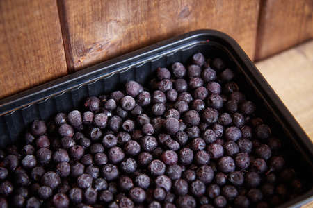 dark black frozen berries lie in a black dish on a wooden table side viewの写真素材