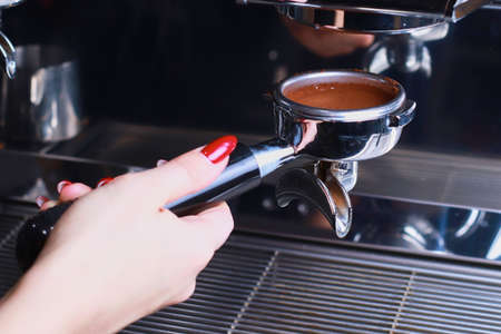 in the female hand is a coffee holder, the coffee beans are poured into the filter and the funnel background is blurredの写真素材