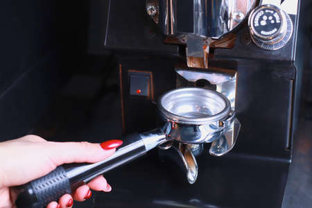 in the female hand is a coffee holder, the coffee beans are poured into the filter and the funnel background is blurredの写真素材