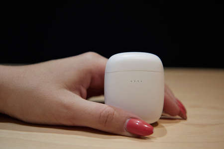 a womans hand holds a case for wireless headphones the background is blurred