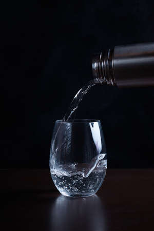 Drinking carbonated water is poured in a stream from a bottle into a transparent glass splashes a blurred backgroundの写真素材