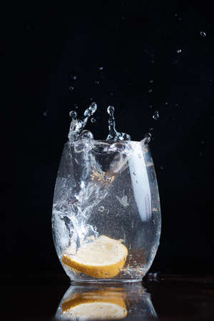 Drinking carbonated water movement drops lemon citrus into a clear glass splashes fly blurred backgroundの写真素材