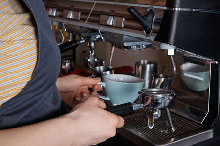 barista prepares and pours coffee into a mug on the coffee machine, close-up, hands of a woman, blurred backgroundの写真素材