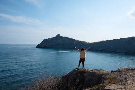 the girl looks at the sea, stands on the shore with her hands raised, a happy person on vacation