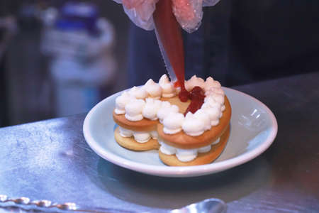 the gloved hands of the chef prepare a cream cake on a shiny table on a plate in the kitchen background out of focusの写真素材