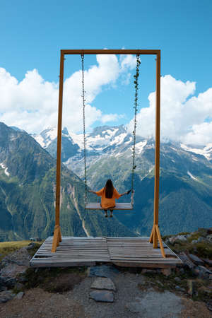 a girl rides a swing in the mountains, a landscape of mountains, alpine meadows and peaks in iceの写真素材