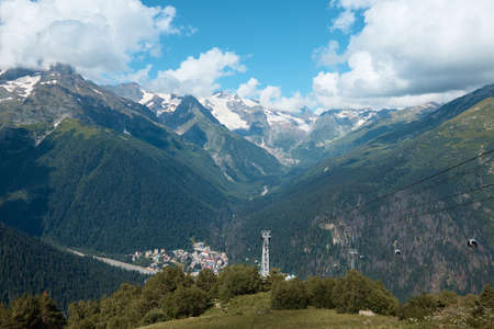 Cable car in the mountains, grass and mountains with glaciers, alpine meadows, village in the mountainsの写真素材