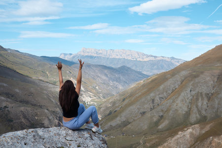 a girl sits on the edge of a cliff and looks into the distance, river gorge, good mood, clouds and a mountain landscapeの写真素材