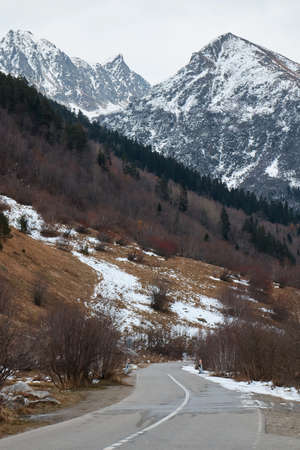 winter landscape, road in the autumn forest, coniferous forest and the first snow, mountains on the...