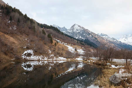 autumn landscape, lake in the mountains, water surface, fallen trees, coniferous forest and the first snow, mountainsの写真素材