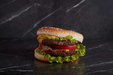 burger with meat and cheese on the table, american cuisine, close-up, tomato, dark background, marble,の写真素材