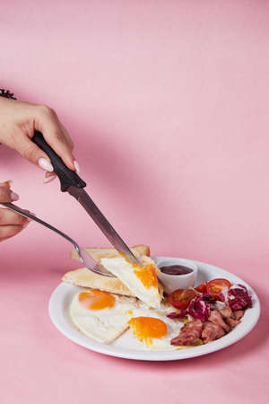 the girl cuts an omelet with a knife, breakfast in a plate, salad and egg, cucumbers and tomatoesの写真素材