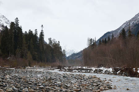mountain landscape in winte, river and rocky shore, mountains and forest on the background, round stones, coldの写真素材