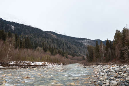 mountain landscape in winte, river and rocky shore, mountains and forest on the background, round stones, coldの写真素材
