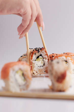a hand and Chinese chopsticks holds a roll over other sushi, a portion of Asian food, rollsの写真素材