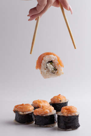 hand and chinese chopsticks, roll falls on the table above other sushi, portion of asian food, rollsの写真素材