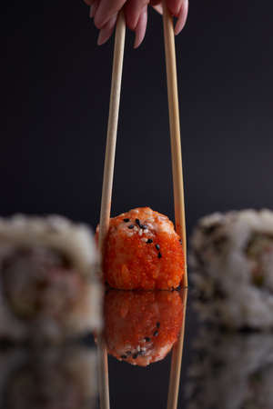 a hand and Chinese chopsticks holds a roll over other sushi, a portion of Asian food, rollsの写真素材