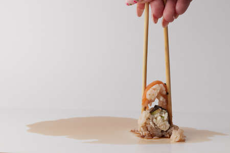 a hand and Chinese chopsticks holds a roll over other sushi, a portion of Asian food, rolls