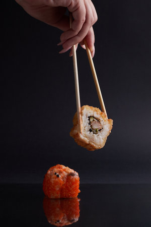 a hand and Chinese chopsticks holds a roll over other sushi, a portion of Asian food, rollsの写真素材