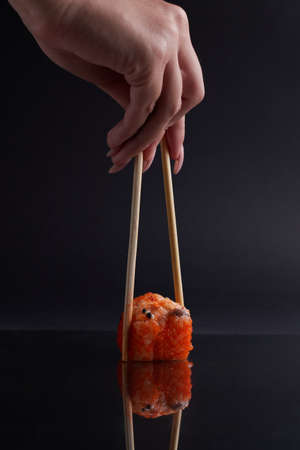 a hand and Chinese chopsticks holds a roll over other sushi, a portion of Asian food, rollsの写真素材