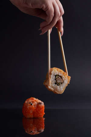 a hand and Chinese chopsticks holds a roll over other sushi, a portion of Asian food, rollsの写真素材