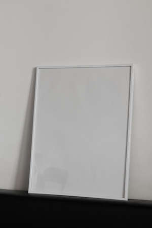Large white photo frame on the floor, mockup, poster on the wall, light background