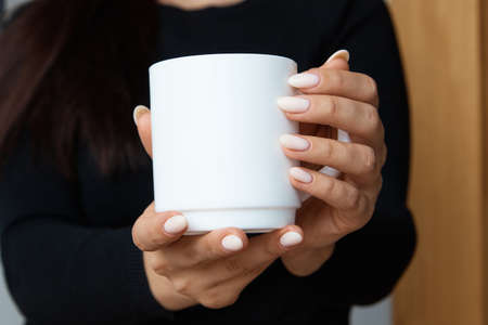 White mug for tea and coffee in the hands of a girl, close-upの写真素材