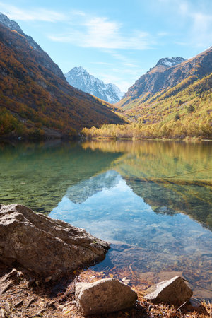 autumn landscape in mountains, lake with clear water, golden trees on slopes of mountains, stone shoreの写真素材